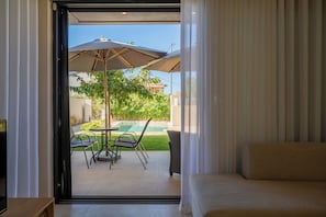 A bedroom with a large window, a bed, and a view of an outdoor patio with a pool and chairs.