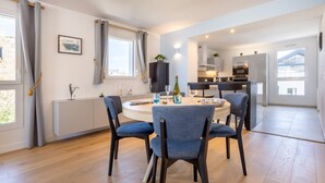Een moderne eetruimte met een ronde tafel, blauwe bekleden stoelen en uitzicht op de keuken op de achtergrond.
