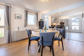 A modern dining area with a round table, blue upholstered chairs, and a view of the kitchen in the background. - Apartment L'instant Suspendu – 2 Private Terraces and Wi-Fi (Concarneau)