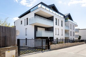 Ein modernes, mehrstöckiges Gebäude mit Balkonen, einem verschlossenen Eingang und blauem Himmel.