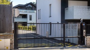 Een omheind toegangspunt tot een gebouw met een moderne architectuur, inclusief een metalen hek en een vrij inzichtelijk pad.