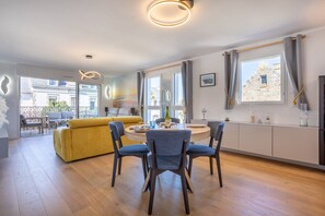 Ein modernes Wohnzimmer mit einem gelben Sofa, einem Esstisch mit Stühlen und einer Küchenzeile mit Fenster.