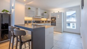 Een moderne keuken met een centraal eiland, barkrukken, inbouwapparatuur en potplanten.