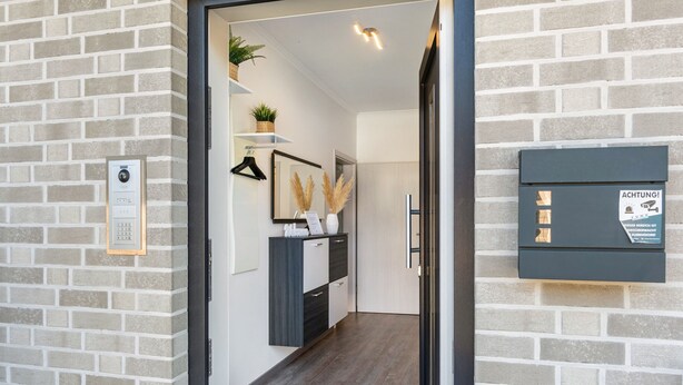 Una entrada de hotel moderna con un muro de ladrillo, un mostrador de recepción, una planta y un buzón.