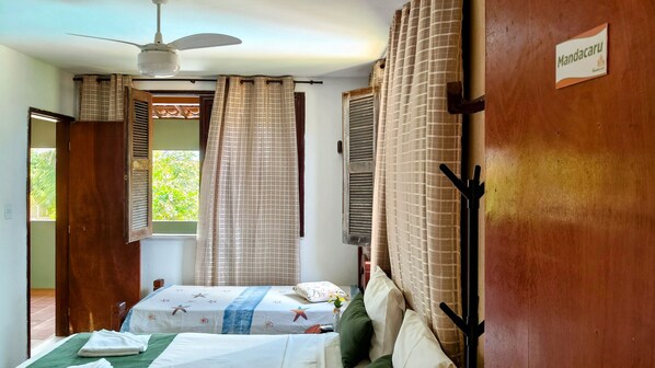 Una habitación con cama, ventilador de techo, ventana con cortinas y un cartel en la pared.