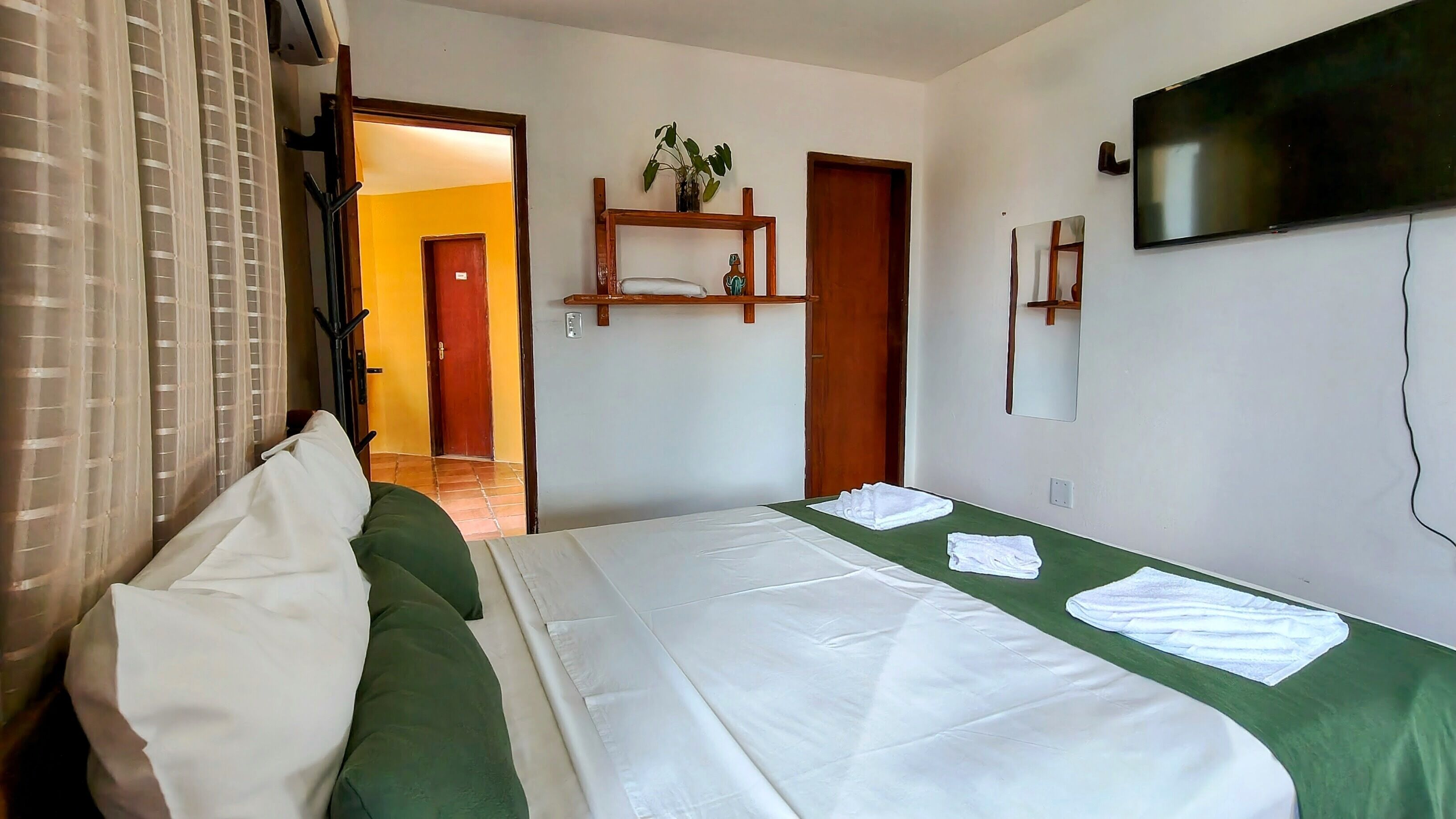 A hotel room with a bed, a TV, a mirror, and a door leading to another room.