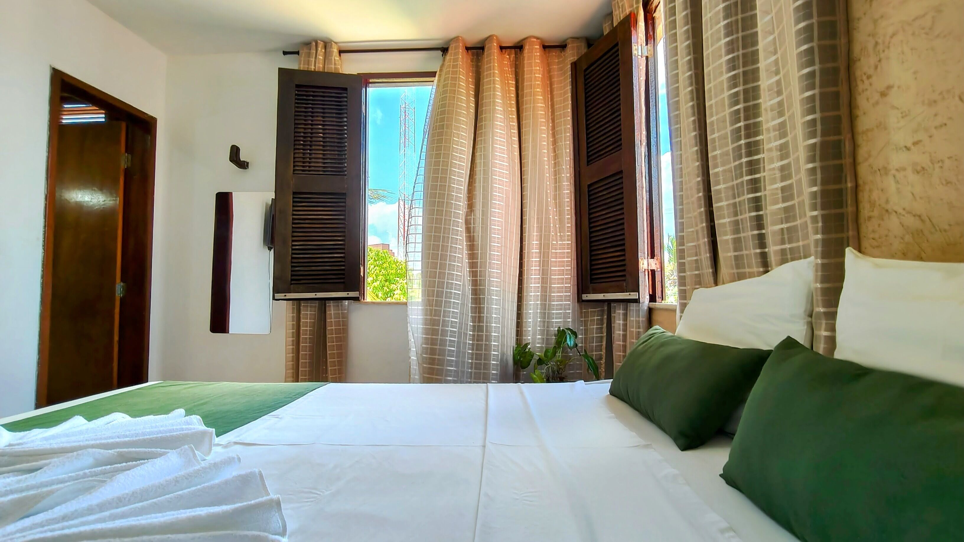 A hotel room with a bed, curtains, a window, and a door.