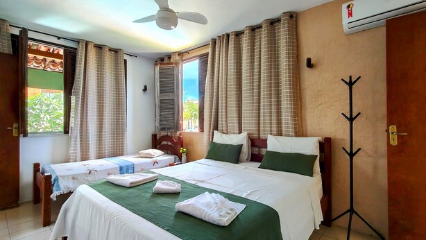 Une chambre d’hôtel avec deux lits, un ventilateur de plafond, un appareil de climatisation, un porte-manteau et une vue sur les palmiers à l’extérieur.