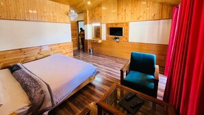 A wooden-paneled room with a bed, a chair, a TV, and a red curtain. - Mountain Green Villa (Manali)