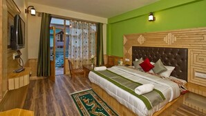 A bedroom with a large bed, a wooden headboard, a television, and a view of a building outside. - Mountain Green Villa (Manali)