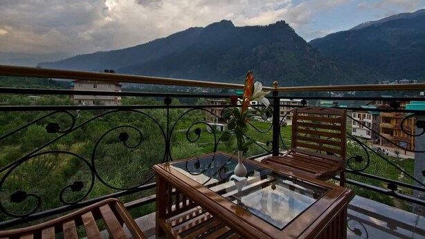 A balcony with a glass table, wooden chairs, and a vase with flowers. - Mountain Green Villa (Manali)