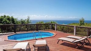 Um deck de madeira com uma banheira de hidromassagem, duas cadeiras de descanso e vista para o oceano.