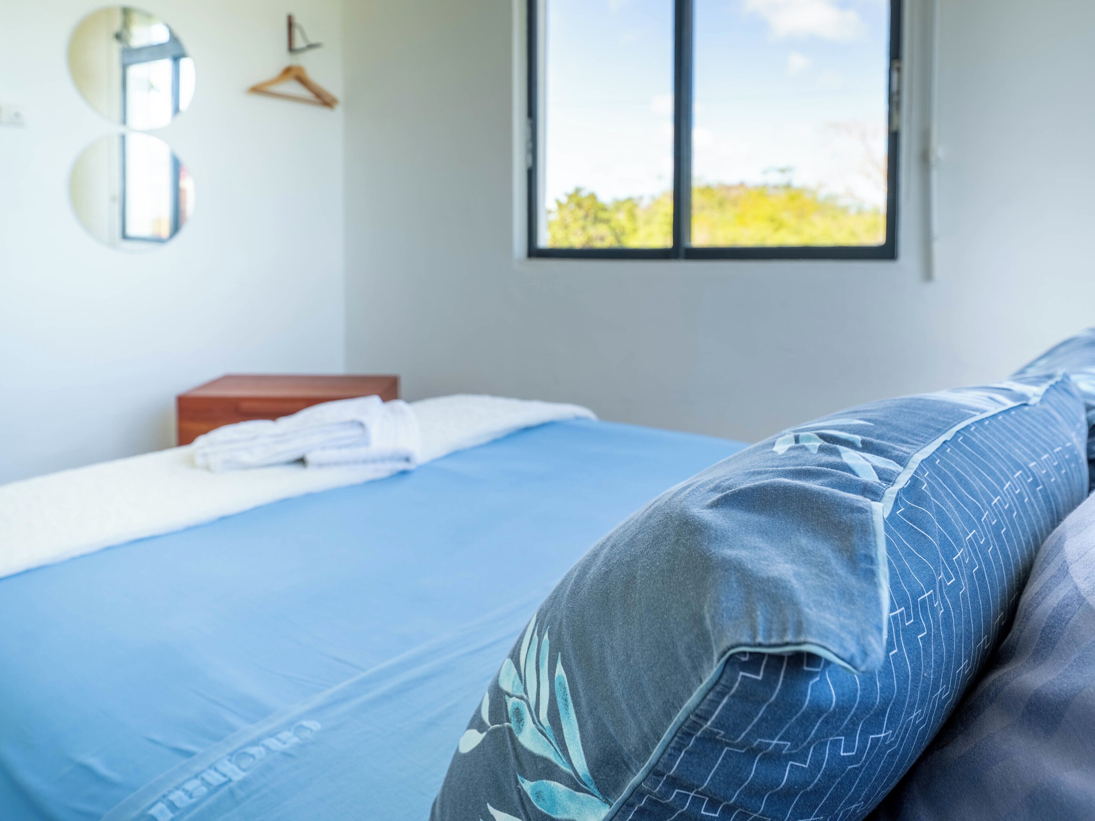 Un dormitorio con cama, ventana y espejo en la pared.