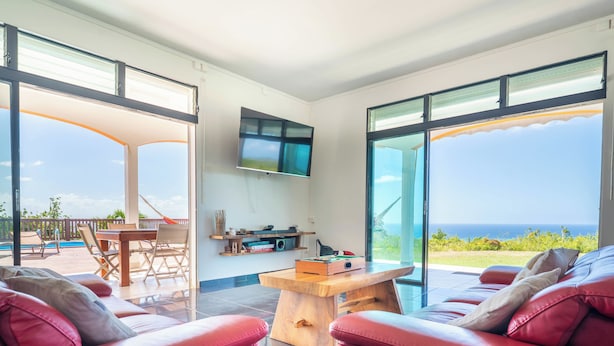Uma sala de estar moderna com vista para a piscina, sofás de couro vermelho, uma mesa de centro de madeira e uma televisão de tela plana.