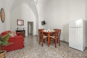 Zona pranzo con tavolo imbandito per quattro persone, un divano rosso, un frigorifero bianco e una TV fissata a parete.