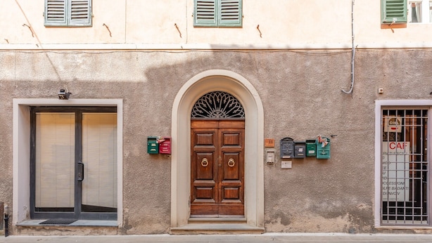 A building with a central arched wooden door, a side door with a metal gate, and mailboxes on the wall. - Casa Ilaria Vicopisano (Vicopisano)