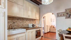 A kitchen with white cabinets, a microwave, and a sink. There is a dining area with a table and chairs. - Casa Ilaria Vicopisano (Vicopisano)