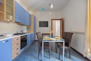 A compact kitchen with blue cabinets, a dining table with chairs, and a window. - Borgagne Apartment by BarbarHouse (Melendugno)