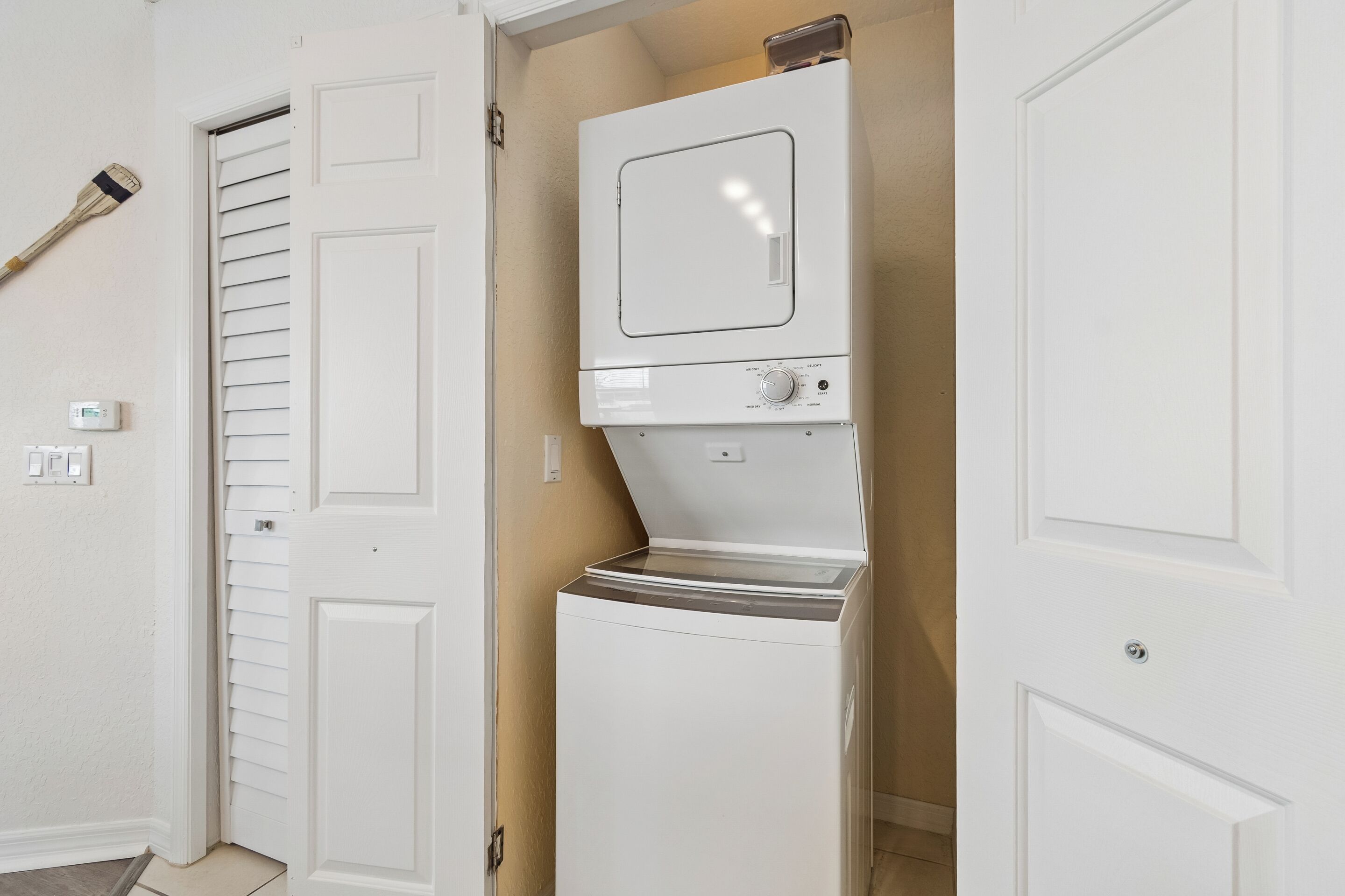 A laundry room with a washer and dryer, a door with a window, and a wall-mounted thermostat.