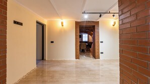 A corridor with a brick wall on one side, a door on the other, and a seating area with chairs and a table in the background. - The Vault Apartment | Unique Stay | Sibiu Center (Sibiu)