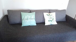 Un sofá gris con dos almohadones decorativos, uno con diseño floral y otro con texto.