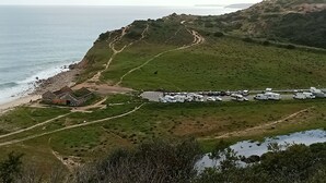 Un paisaje costero con una carretera que lleva a un edificio, un estacionamiento con vehículos y una playa.
