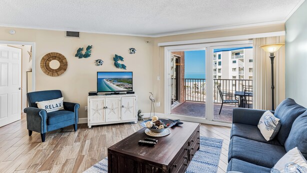 A living room with a sofa, armchair, coffee table, TV, and a balcony with a view. - Family Friendly w/ Balcony and Shared Pool BC1314 (Indian Shores)