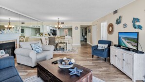 A living room with a fireplace, a television, and a dining area in the background. - Family Friendly w/ Balcony and Shared Pool BC1314 (Indian Shores)