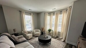 A living room with a sofa, armchair, coffee table, and curtains. - Chic Westerville Retreat Near Uptown Westerville • Walk to Coffee • Sleeps 6 (Westerville)