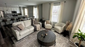 A modern living room with a sofa, armchairs, a coffee table, and a kitchen in the background. - Chic Westerville Retreat Near Uptown Westerville • Walk to Coffee • Sleeps 6 (Westerville)