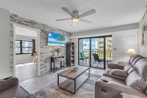 Ein modernes Wohnzimmer mit einer Couch, einem Couchtisch, einem Deckenventilator und Blick ins Freie.