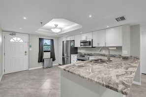 A modern kitchen with white cabinets, stainless steel appliances, and a marble countertop. - Madeira Place #201 (Madeira Beach)