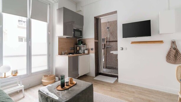 A modern kitchen with a microwave, oven, and sink, a television mounted on the wall, and a sliding glass door leading to a shower area. - Studio Solo - Opera Galeries Fayette - 1 Pax (Paris)