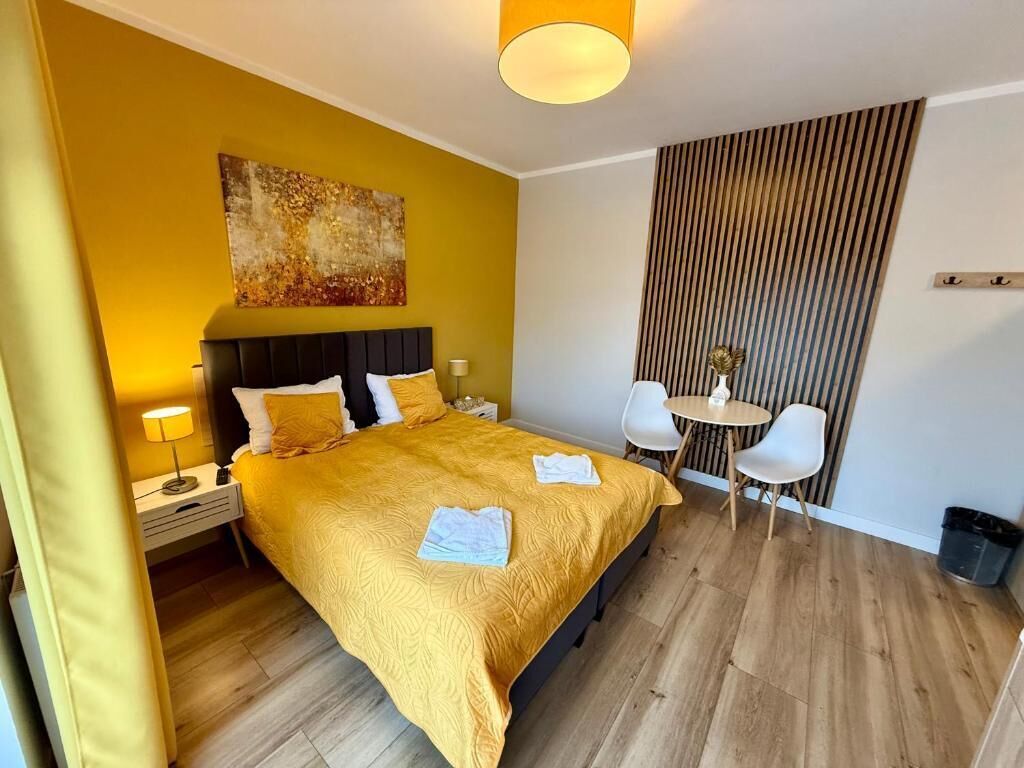 A hotel room with a bed, bedside tables, a small round table with chairs, a painting on the wall, and a vertical striped panel.