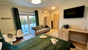 A modern hotel room with a bed, a desk, a television, a chair, and a view of the outdoors. - Pokoje Balticus Mrzeżyno (Mrzeżyno)