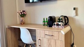 A small, modern room with a wooden desk, a white chair, a flat-screen TV, and a coffee maker. - Pokoje Balticus Mrzeżyno (Mrzeżyno)