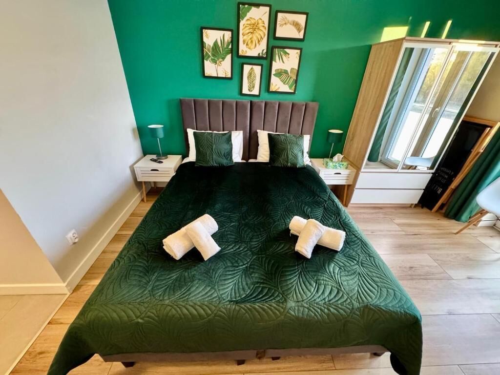 A bed with a dark green quilt, a wooden headboard, and a wall with framed tropical leaf art.