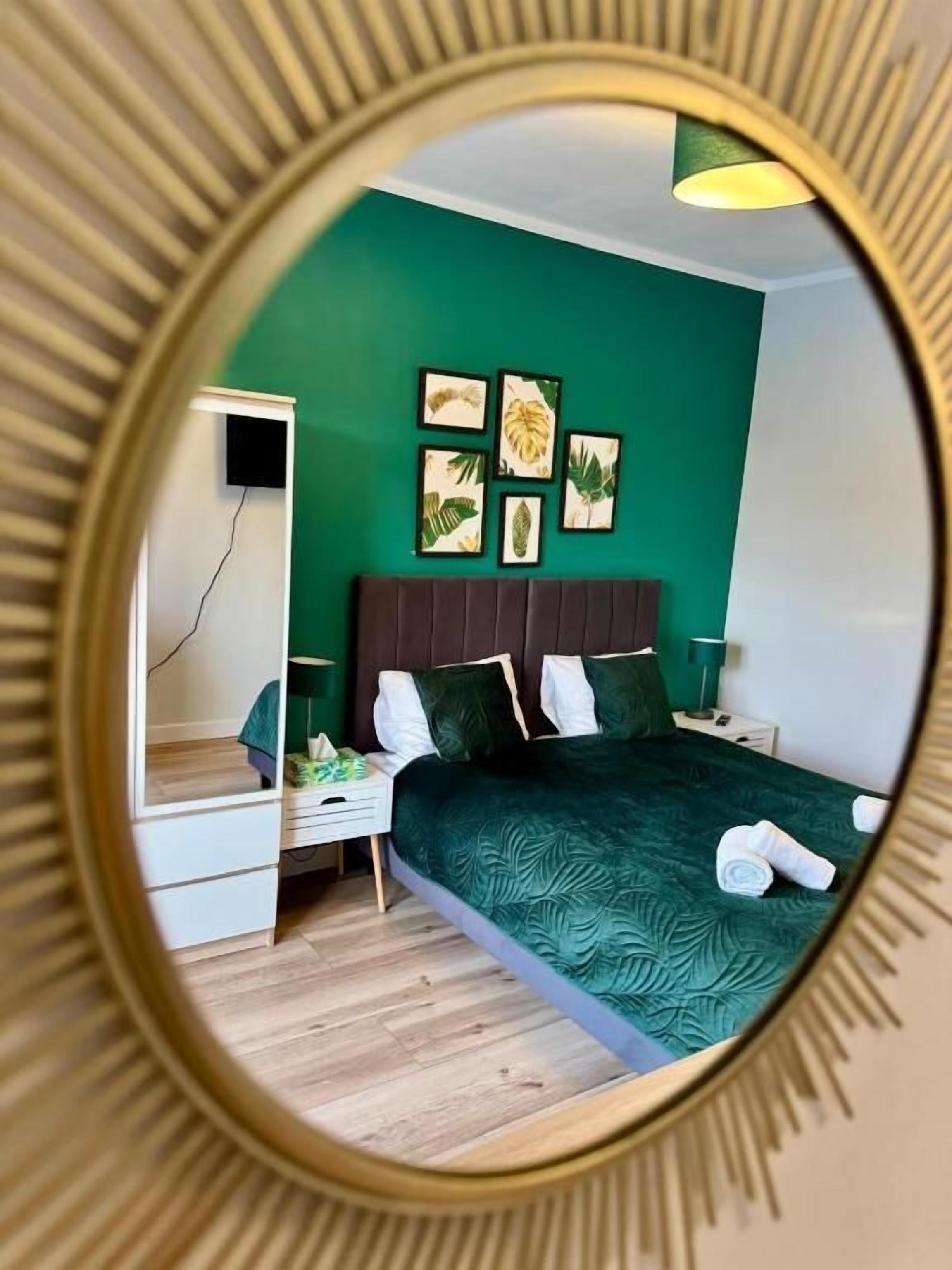 A bedroom with a green wall, a bed with a dark green bedspread, a headboard, and a nightstand with a lamp.