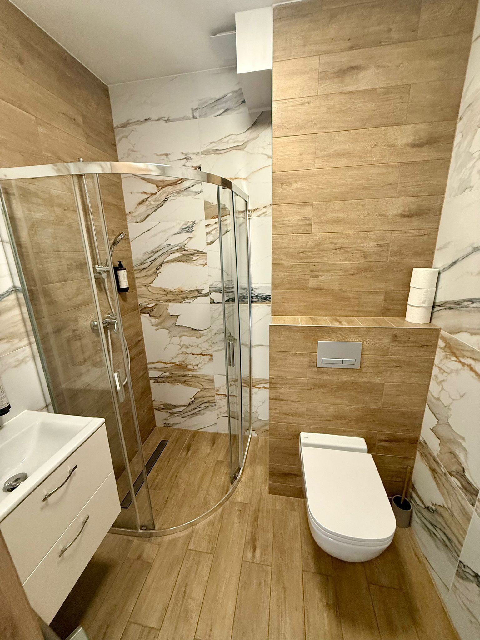 A modern bathroom with a glass shower enclosure, a white toilet, and marble-patterned walls.