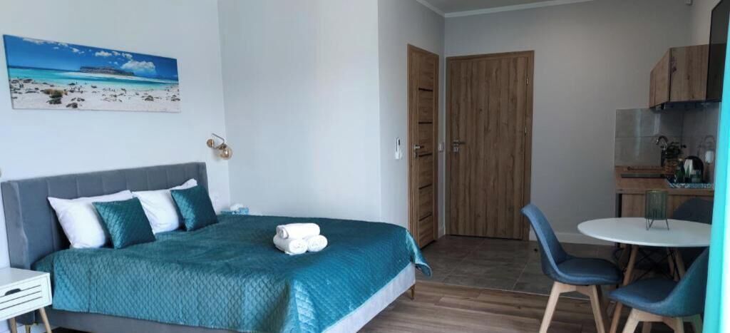A bedroom with a bed, a desk, a chair, a dining table, and a kitchen area.