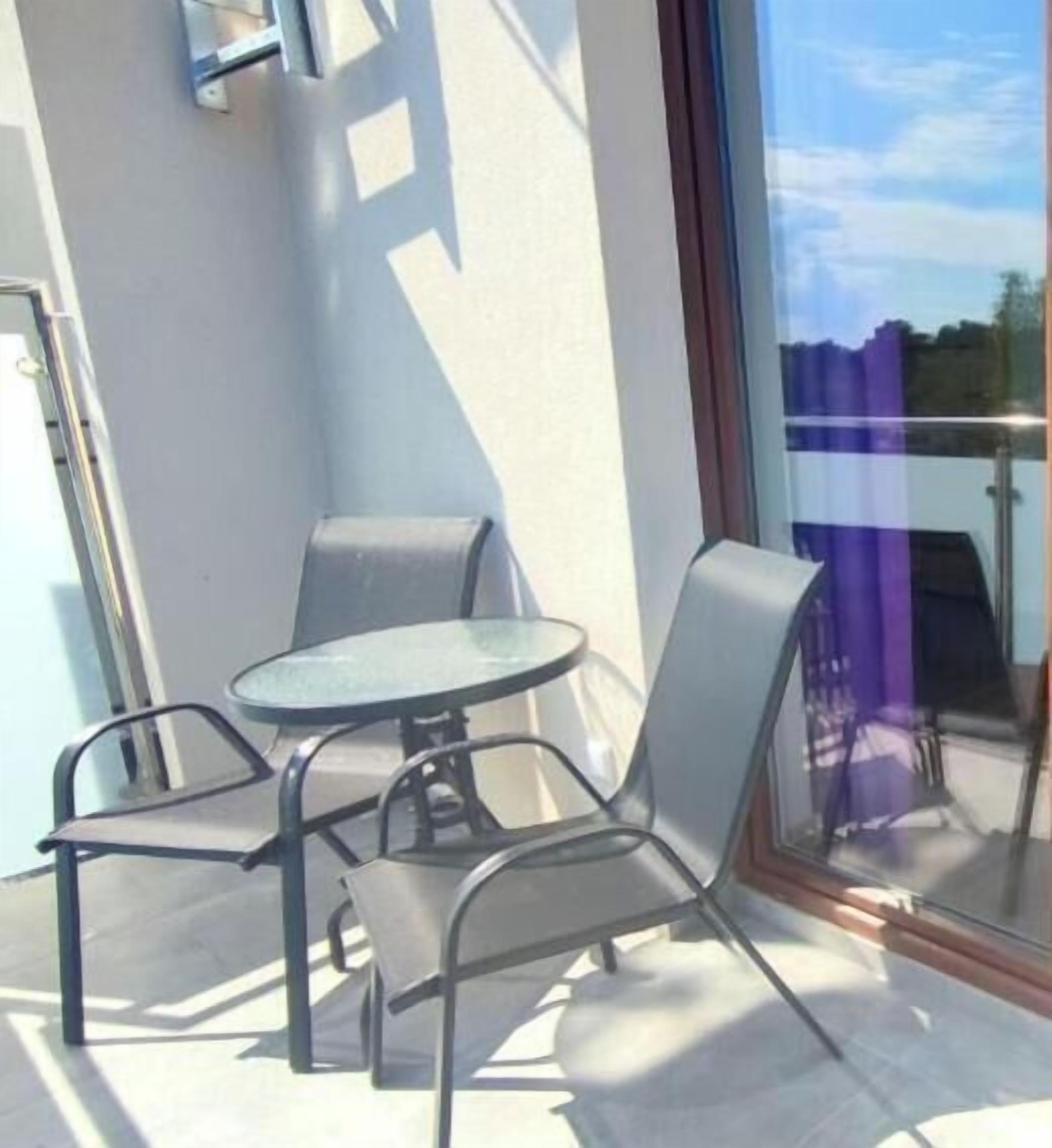 A balcony with two chairs and a small table, a glass door, and a metal railing.