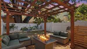 Una pergola in legno con luci a tendina, un braciere e posti a sedere all'aperto.
