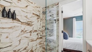 Un bagno moderno con pareti in marmo, box doccia in vetro e un letto con vista.
