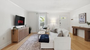 Un soggiorno moderno con una TV a schermo piatto, divani bianchi, un tavolino da caffè, un tappeto decorato e un mobiletto contenitore in legno.