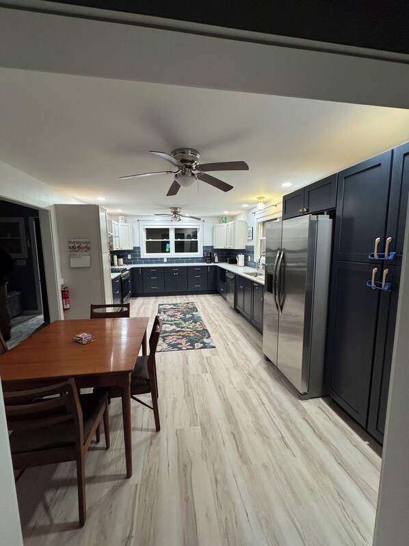 A modern kitchen with dark cabinets, a stainless steel refrigerator, and a ceiling fan.