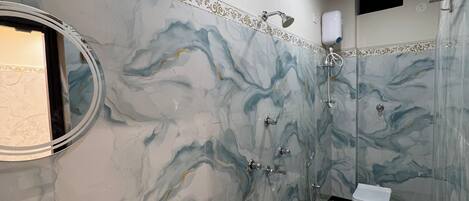 A bathroom with a marble wall, a sink, a toilet, and a shower.