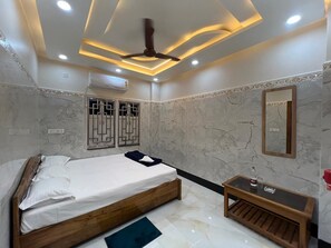 A bedroom with a bed, a bedside table, a mirror, and a ceiling fan. - JALANGI EMPIRE (Mayapur)