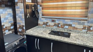 Eine kleine Küche mit Granit-Arbeitsplatte, hängender Küchenausstattung und einer Steinwandverkleidung.