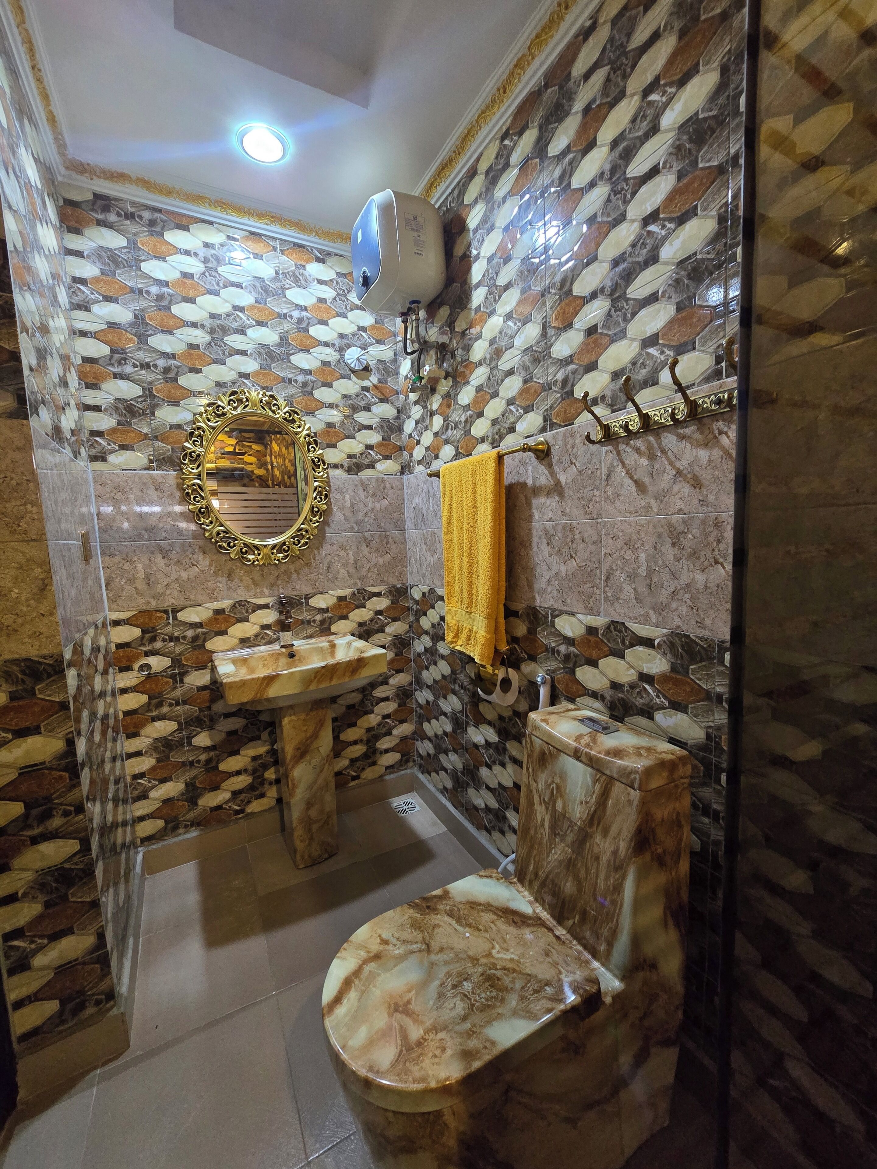 A bathroom with a marble sink, toilet, and shower area, featuring a patterned tile wall and a gold-framed mirror.
