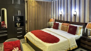 Ein Hotelzimmer mit einem großen Bett, einem Kleiderschrank, einem Spiegel, einer Chandelüster und gestreiften Vorhängen.